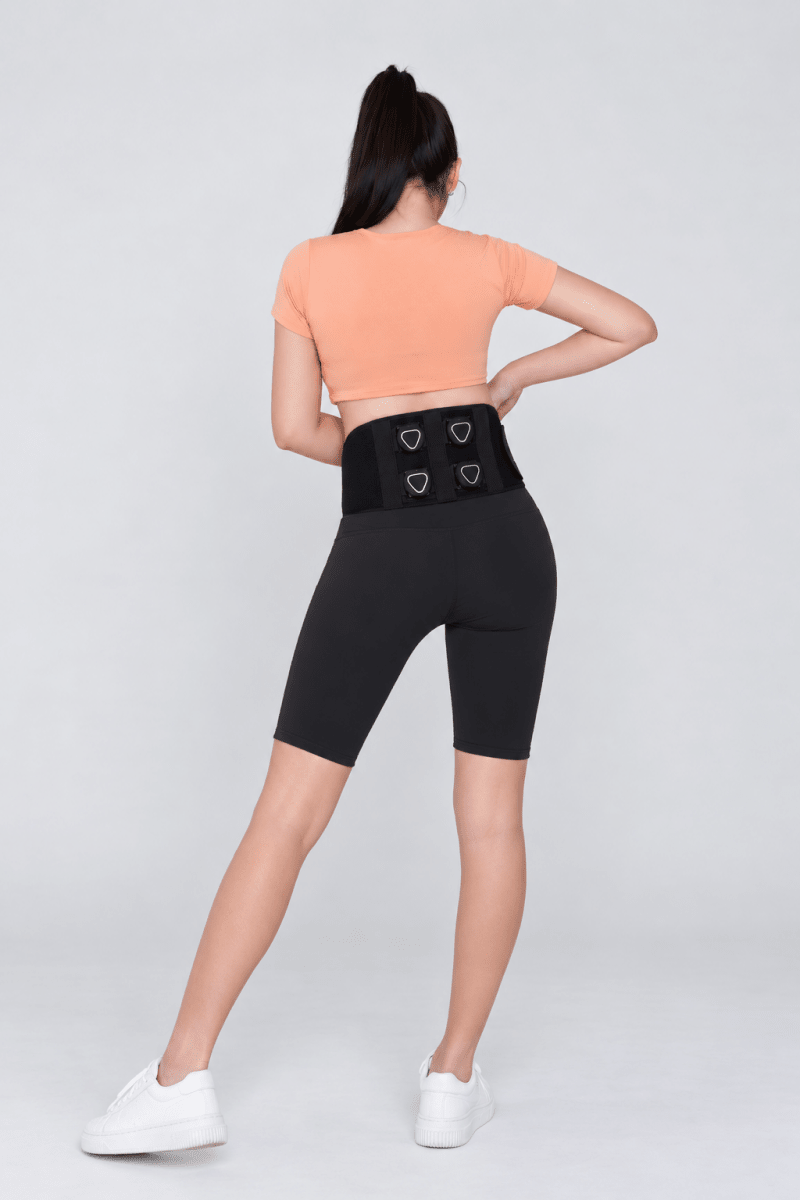 A woman wearing Aalok Band Quad, a peach top, and black shorts designs on a light background
