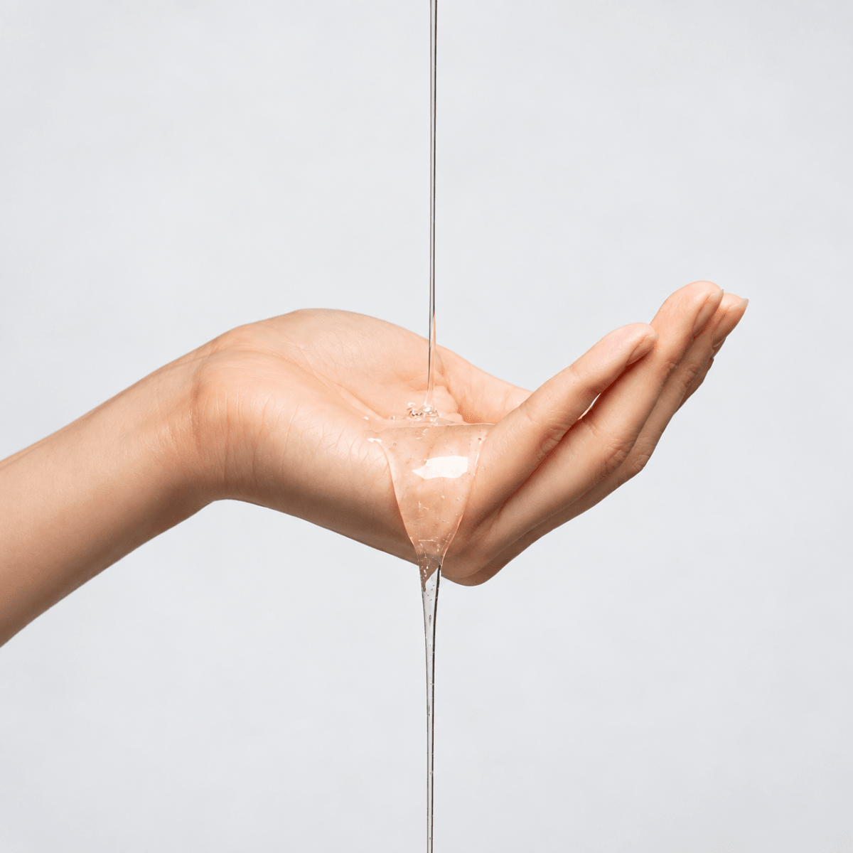 Hand with a small amount of liquid shampoo dripping from it against a light background