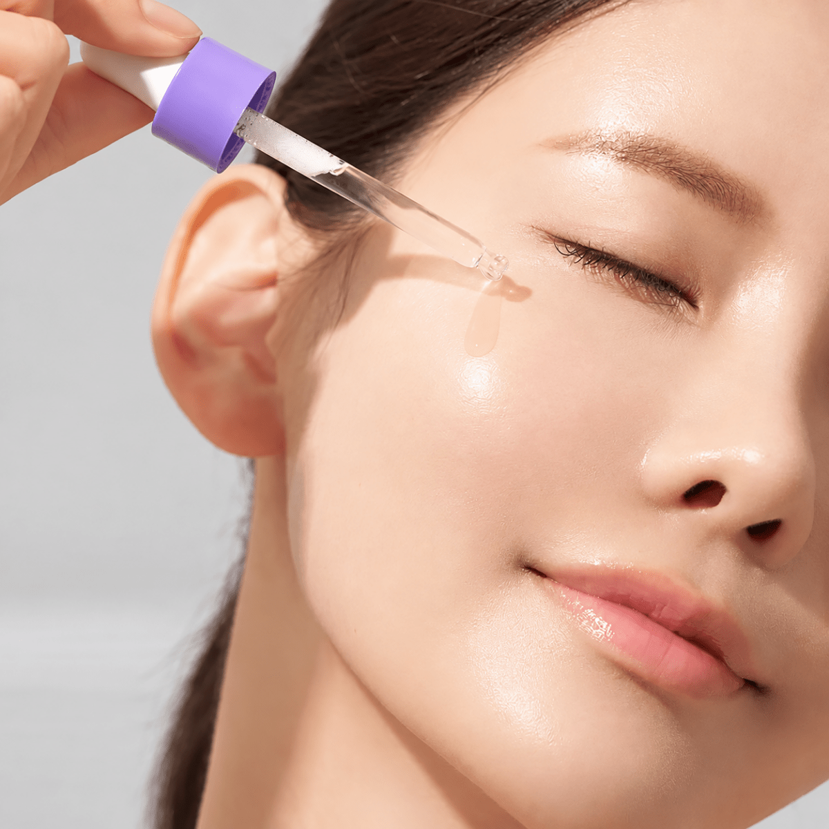Close-up of a woman applying Ultra Hydro Glow Essence to her face with a dropper.