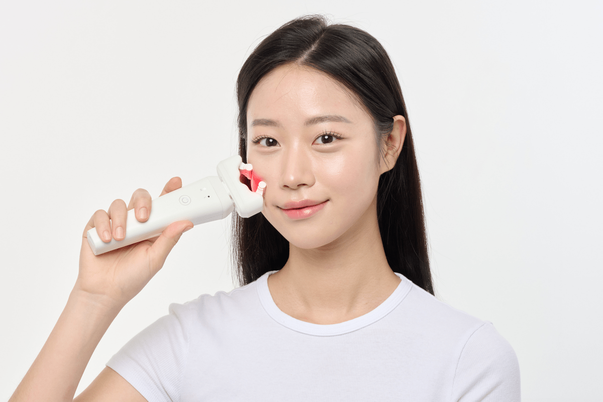 Woman using an Aalok ULTRA Olla on her cheek against a plain background