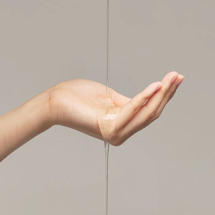 Hand with a small amount of liquid shampo dripping from it against a neutral background

