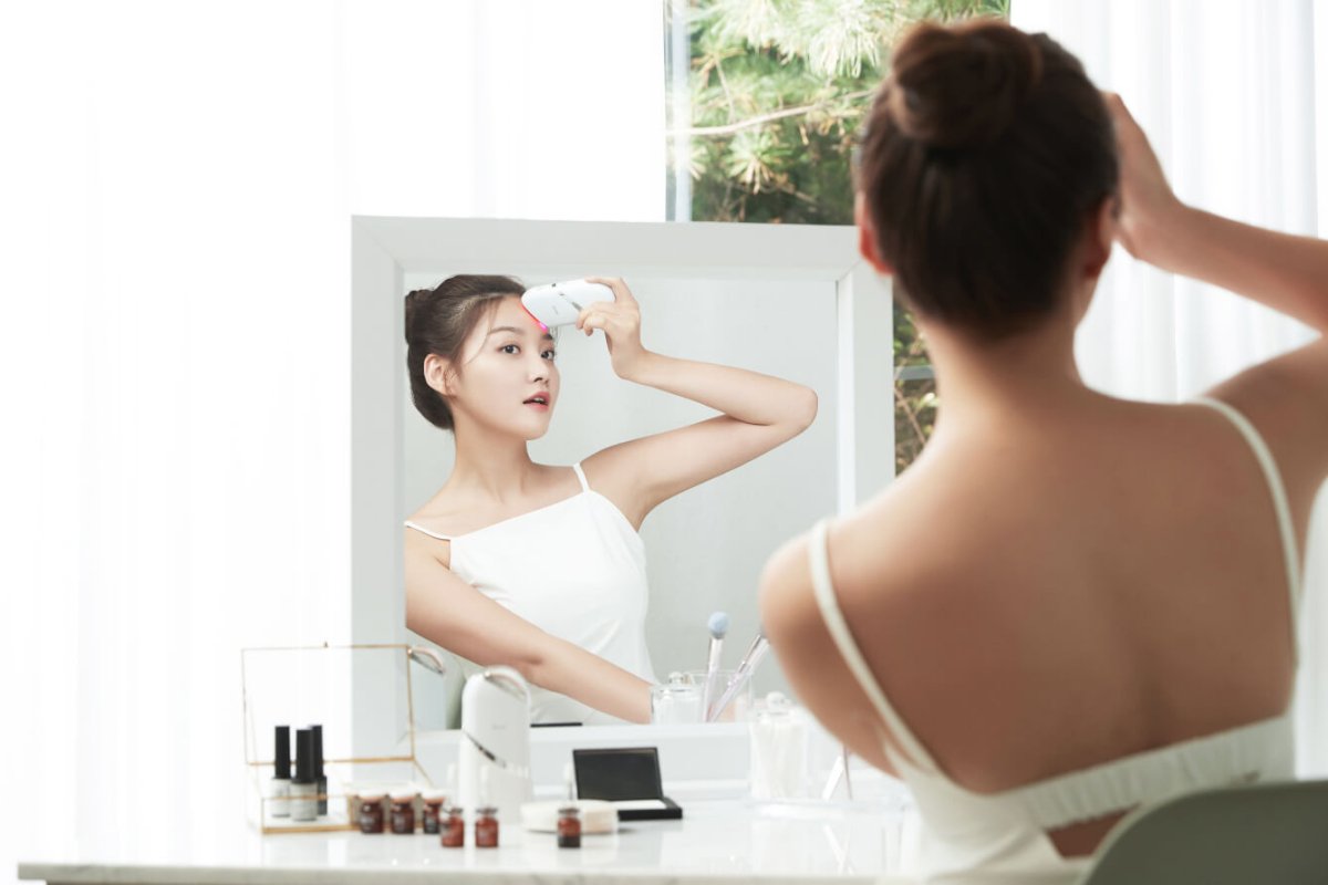 A woman using Aalok Snowfit in her face in front of a mirror with a reflection showing another woman.