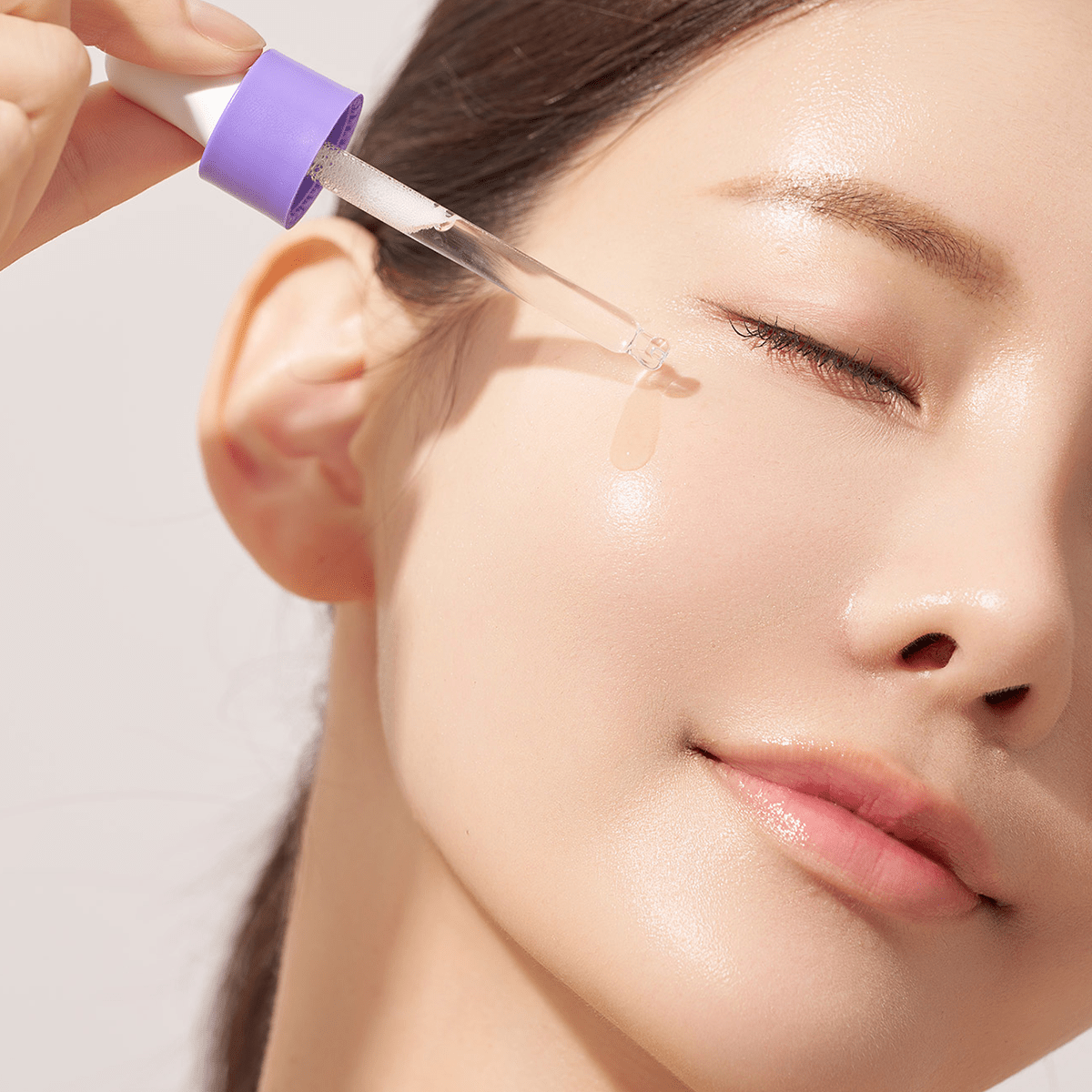 Close-up of a woman applying Aalok Ultra Hydro Glow Essence to her face with a dropper.